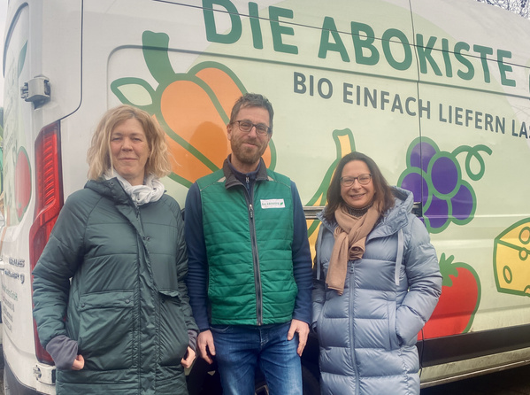 KI generiert: Drei Personen vor einem Lieferwagen mit "DIE ABOKISTE" und Gemüsemotiven. Text: "BIO EINFACH LIEFERN."