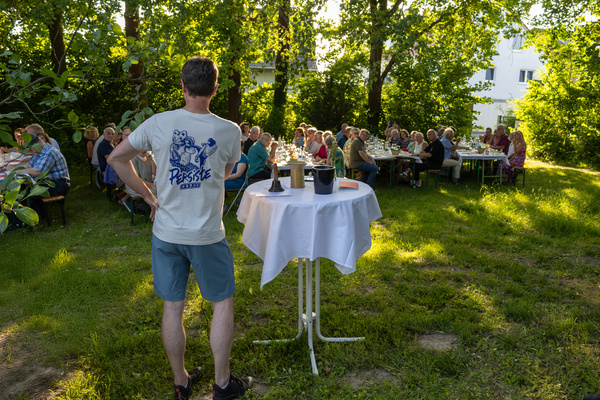 KI generiert: Eine Gruppe von Menschen sitzt draußen an Tischen, im Vordergrund ein Tisch mit Getränken.