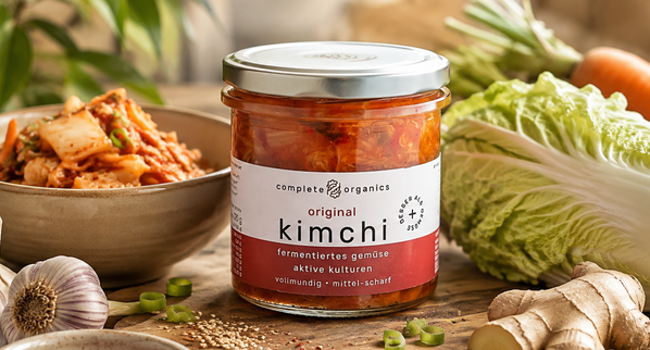 KI generiert: Ein Glas Kimchi mit frischem Gemüse und Gewürzen umgeben. Text: "complete organics original kimchi".