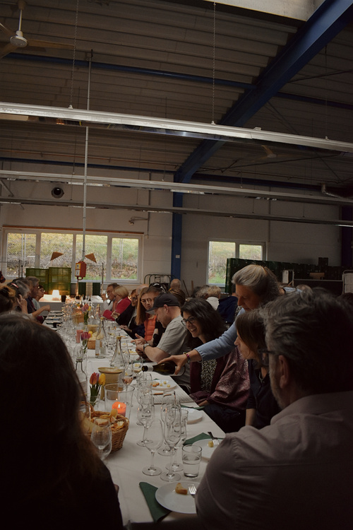 KI generiert: Personen sitzen an einem langen, gedeckten Tisch in einer Halle und essen gemeinsam.
