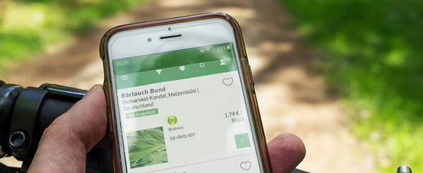 KI generiert: Ein Smartphone zeigt eine App mit Bärlauch-Angeboten. Text: "Bärlauch Bund, 1,79 €/Stück".