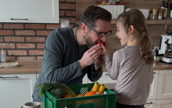 KI generiert: Ein Mann und ein Kind teilen liebevoll einen Apfel in einer Küche mit frischem Obst und Gemüse im Vordergrund.