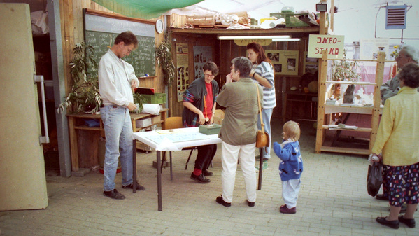 KI generiert: Ein Marktstand mit mehreren Leuten; ein Schild trägt die Aufschrift "INFO-STAND".