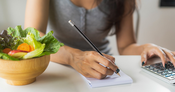 KI generiert: Eine Person notiert etwas, während sie neben einer Schüssel Salat sitzt.