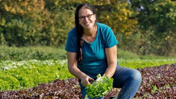 KI generiert: Eine Frau kniet auf einem Feld und hält frischen Salat in der Hand.