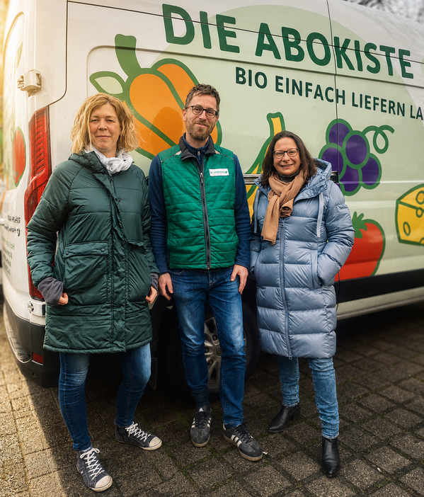 KI generiert: Drei Personen stehen vor einem Lieferwagen mit der Aufschrift "DIE ABOKISTE - BIO EINFACH LIEFERN LASSEN".