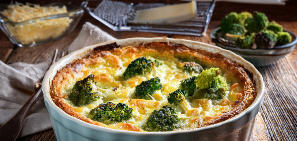 KI generiert: Eine Brokkoli-Quiche in einer Auflaufform auf einem Tisch, umgeben von Käse und Brokkoli.