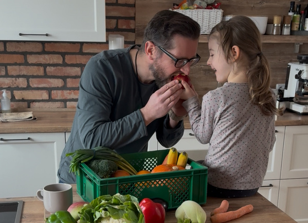 KI generiert: Ein Mann und ein Kind teilen einen Apfel in einer Küche mit Gemüsekorb.