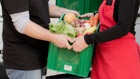 KI generiert: Zwei Personen halten zusammen eine Kiste mit frischem Obst und Gemüse.