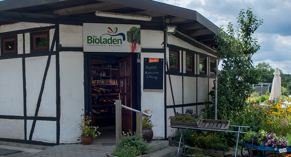 KI generiert: Kleiner Bioladen mit offenem Eingang; Tafeltext: "demeter degustation Mittwoch 5€ / 1g".