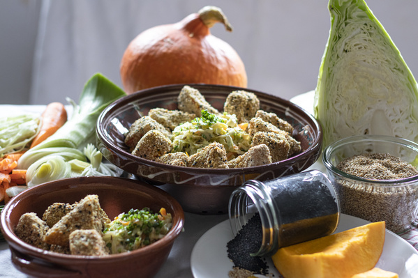 KI generiert: Das Bild zeigt Schalen mit panierten Gemüsestückchen und frischem Krautsalat, umgeben von frischen Zutaten wie Kürbis und Kohl. Daneben sind Gewürze und weiteres Gemüse zu sehen.