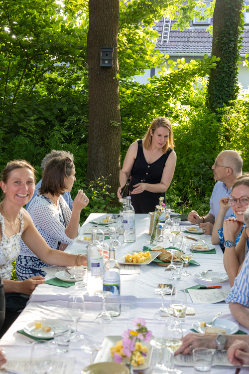KI generiert: Menschen sitzen an einem draußen gedeckten Tisch beim gemeinsamen Essen.