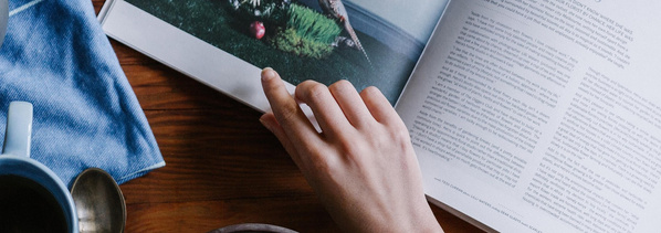 KI generiert: Eine Hand blättert in einem Buch oder Magazin, daneben eine Tasse mit Getränk. Kein sichtbarer Text.