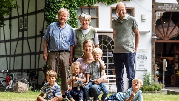 KI generiert: Familie sitzt lächelnd auf einer Wiese vor einem Gewächshaus.