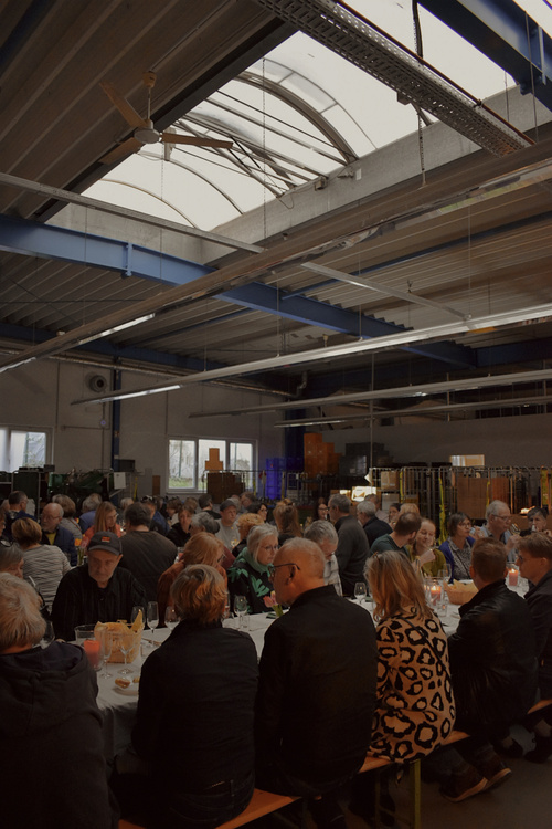 KI generiert: Eine große Gruppe von Menschen sitzt in einer Halle an langen Tischen und isst zusammen.
