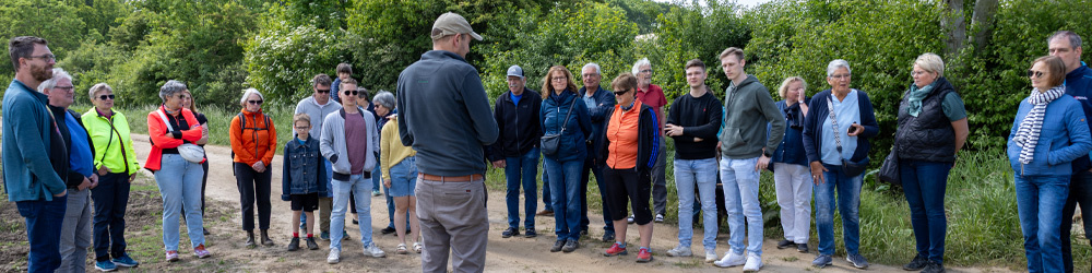 KI generiert: Eine Gruppe von Menschen steht im Freien und hört einer Person zu.
