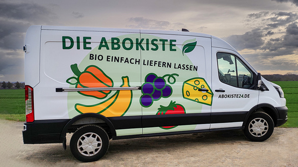 KI generiert: Ein Lieferwagen mit Obst- und Käseabbildungen, beschriftet mit "DIE ABOKISTE BIO EINFACH LIEFERN LASSEN".
