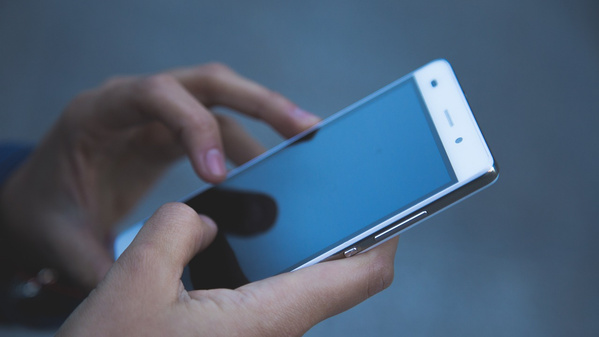 KI generiert: Das Bild zeigt eine Person, die ein Smartphone in den Händen hält. Der Fokus liegt auf dem Gerät und den Händen, während der Hintergrund unscharf ist.